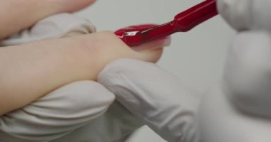 Lateks eldivenli kadın manikürcü kadın tırnaklarını kırmızı ojeyle kaplıyor. Kadın kuaför salonu ziyaretçisi tırnak ameliyatından sonra incelikli ve göze çarpan sonuçları bekliyor. Macro Nail tedavisi. Kapat..