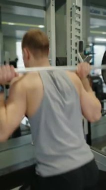 Genç bir erkek sporcu yoğun bir şekilde spor salonunda antrenman yapıyor, halter kaldırıyor, güç ve kararlılık gösteriyor. Salonda Halter Ağırlıklarıyla Sıkı Çalışan Genç Adam. Dikey video.