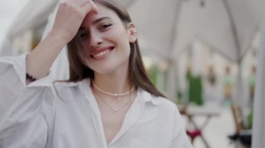 Neşeli genç bir kadın açık bir kafede güneşli bir günün tadını çıkarıyor. Gülüşü mutluluk ve güven saçıyor. 