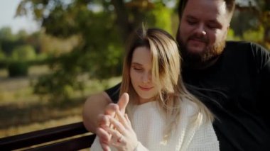 Neşeli bir adam ve kadın birlikte gülüyor ve sıcak bir anın tadını çıkarıyor. Parktaki yemyeşil ağaçlarla çevrili bir bankta oturuyorlar. El ele tutuşurlar, sevgi ve mutluluk gösterirler. 