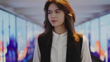 Kendine güveni olan genç bir kadın parlak bir ofis koridorunda duruyor ve kurumsal bir ortamda profesyonel bir atmosfer yayıyor. Modern Ofis Koridorunda Genç Profesyonel Kadın