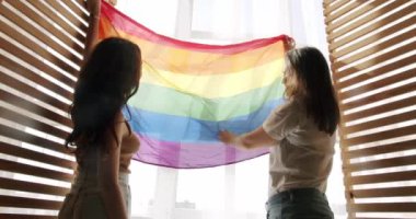 Çift, Lgbt ve lezbiyen kadınlar evde. Sarılın, gülümseyin ve bayrak sallayın. Aşk ve öpücük, iki kadın el ele tutuşarak sevgi ve desteği paylaşıyor. Yaşam tarzı ve ilişkiler. LGBT kavramı