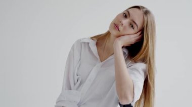 Sarı saçlı, beyaz gömlekli, dingin görünümlü güzel bir kadının portresi. Moda ve yaşam tarzı için ideal. Sarı saçlı genç manken tabure gri duvarda oturuyor.