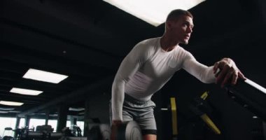 Beyaz spor kıyafetli kaslı adam iyi donanımlı bir spor salonunda ağırlık kaldırıyor. Güç ve kararlılık gösteriyor. Modern Spor Merkezi 'nde Erkek Dambılları Kaldırma Odaklı