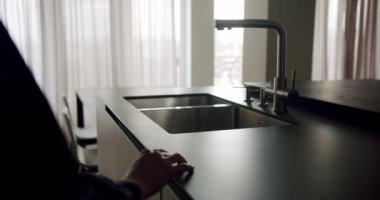 Modern bir mutfağın, koyu tezgahlara ve şık bir lavabo musluğuna odaklı gösterişli, gösterişli, minimalist bir tasarımı. Modern Mutfak Detayları Parlak Tezgahlar ve Minimalist Tasarım