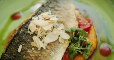 Yavaş çekim deniz levreği, bbq sebzeleriyle servis edilir. Yakın çekim. Üst Manzara. Patates püresi ve sebzeli güzel dekore edilmiş beyaz balık parçası yeşil tabak ve beyaz arka planda dönüyor..