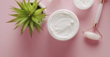 Üst görünüm beyaz şişe, serum, palmiye yapraklı pembe silindir stüdyoda pembe arka planda kozmetik için dönüyor. Kremalı kozmetik kavanozu. Farklı kozmetik şişelerden oluşan bir grup. Üst görünüm.