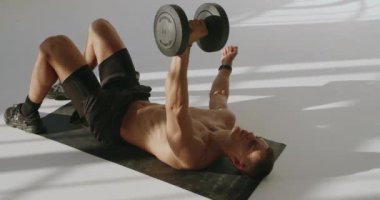 Dambıllar ve Odaklanma ile Stüdyoda Atletik Genç Adam Eğitimi. Spor salonunda dambıllarla antrenman yapan atletik bir adam güç ve konsantrasyon gösteriyor..