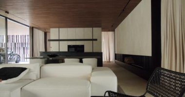 Elegant modern living room with clean lines and sophisticated design, featuring plush white sofas, wooden ceiling, and a stunning view of a supercar through full-length windows.