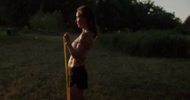 Sporty woman has workout outdoors and training with resistance band in hands. Female exercising outside in morning at sunrise. Athletic woman goes in for sports with resistance band.