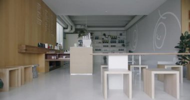 Bu resimde, minimalist bir tasarımı olan, ahşap mobilyaları ve yatıştırıcı nötr renk paleti olan modern bir kahve dükkanı yer alıyor. İçerisi geniş ve parlak.