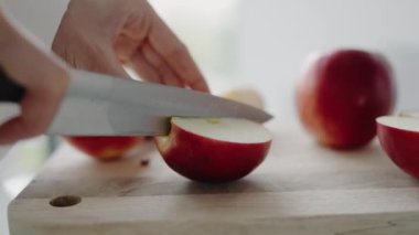 Taze kırmızı bir elmayı tahta bir kesme tahtasının üzerinde bıçakla keserken yakın plan çekilmiş bir fotoğraf. Görüntü sağlıklı beslenme ve yemek hazırlamanın özünü yakalıyor. Kırmızı Elmaları Kesen Kişi
