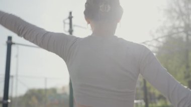 Güneşli bir parkta kollarını esneten bir bayan sporcu. Kentsel bir ortamda zindelik ve sağlığa odaklan. Güneşli şehir parkında kollarını açan genç bir kadın.