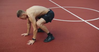 Atletik adam dışarıda antrenman yapıyor ve spor sahasında zıplayarak ve iterek burpee egzersizi yapıyor. Spor, sağlık, spor, spor, spor. Dayanıklılık, genç sporcu burpee egzersizi yapıyor.