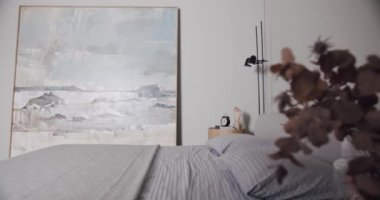 Minimalist bir dairede yatak odası, beyaz tonlarda, modern büyük resim ve siyah lamba ile. Rahat minimalist iç mekan. Şık ev, otel odası, modern mobilya, modern ev tasarımı.