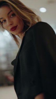 Kalın kırmızı ruj sürmüş, kendine güveni tam bir kadın portresi ve şık bir siyah ceket giymiş, doğrudan kameraya bakan bir ev ortamında. Kırmızı ruj sürmüş kendine güvenen bir kadın. Dikey.