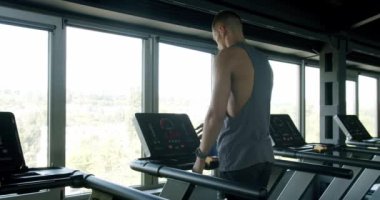 İyi donanımlı bir spor salonunda koşu bandında koşan genç bir erkek manzaralı bir şehir manzarasına bakıyor. Zindelik ve yaşam tarzı dengesini yakalamak. Modern Spor Salonu 'nda Koşan Fit Genç Adam