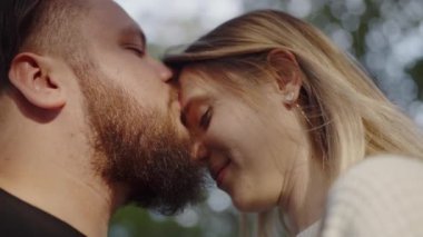 Sakallı bir adamın sarışın bir kadını nazikçe öpmesi ve doğal bir ortamda yakınlık ve şefkat göstermesi gibi hassas bir an. Sevgili Çiftin Yakın Çekimi Dışarıda Nazikçe Öpüşüyor