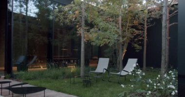 Doğa ile çevrili, rahat şezlonglar ve güzel manzaralı bahçeyle donatılmış modern bir evin zarif dış mekanı. Lush Garden ve Rahatlatıcı Sandalyeleri olan Modern Ev Dışı