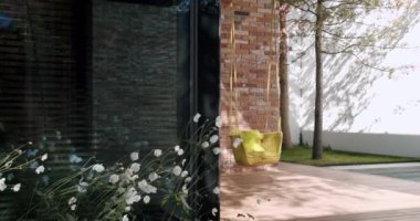 Zarif bir evde sakin bir ortam. Yansıtıcı havuzun yanında yeşil minderleri olan rahat bir rattan sallanan sandalye. Büyüleyici çiçek dokunuşları olan tuğla bir duvara dayanıyor. Modern Ev Bahçesi