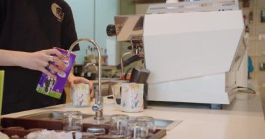 Modern bir kahve dükkanında arka planda profesyonel bir kahve makinesi olan bardaklara süt döken bir baristanın resmi. Çağdaş bir ortamda gündelik profesyonellik.