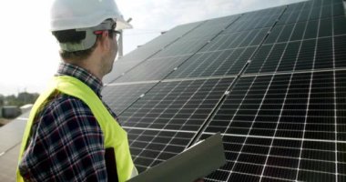 Teknisyen güneş enerjisi kurulumundaki panelleri kontrol ederek güneş enerjisi alanındaki güneş pili çiftliğini inceliyor. Güneş pilleri geleceğin önemli bir yenilenebilir enerjisi olacak..