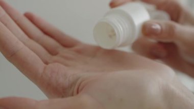 Beyaz ilaç şişesinden dağıtılan beyaz hapları tutan ve kendine bakım ve sağlığa odaklanan bir kişinin yakın çekimi. El Doğal Işıkta Beyaz Şişe 'den Bir Hap Alırken