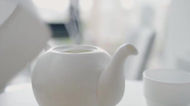 Parlak bir mutfak ortamında beyaz bir çaydanlık ve uyumlu bir fincan çay severler için sakin ve davetkar bir ortam yaratıyor. Ev, konukseverlik ve rahatlama kavramları için mükemmel..