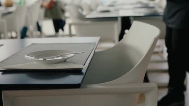 Beyaz tabak ve gümüş takımlı şık bir restoran masası. Çağdaş bir yemek ortamında minimalist ve temiz bir tasarım. Restoranda boş sandalyeyle servis masasına yakın çekim.