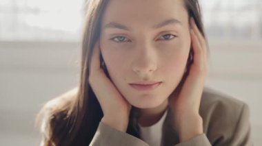 Stüdyoda beyaz gömlekli ve kahverengi ceketli güzel bir esmer kadın var. Güzel bir kadının pürüzsüz ve sağlıklı bir teni var. Güzel kız, izole edilmiş beyaz arka planda gülümsüyor..