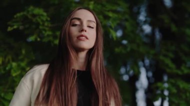 Açık havada duran ve doğanın huzurunun tadını çıkaran sakin saçlı bir kadının portresi. Arka planda yemyeşil yapraklar var. Uzun Saçlı Serene Woman Doğa 'da Dinleniyor