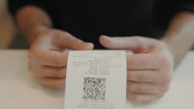 Birisi detaylı bir makbuzu QR koduyla inceliyor. Konferansta eller ve basılı kağıt üzerinde duruluyor, bir anlık mali işlem ya da gözden geçirme anı yakalanıyor. Elektronik Fatura İncelemesi