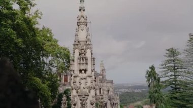 Portekiz 'de yemyeşil ağaçlarla çevrili tarihi bir şatonun heybetli taş kulesi ve bulutlu bir gökyüzüne karşı kurulmuş. Manzara arka planda uzanır..