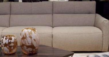 Modern gri ve bej kumaş kanepe. Yastıklı tekstil döşeme kanepesi. Modern apartman güzel bej kanepe minimalist oturma odasında lamba, masa. Ahşap duvarlı İskandinav iç mimarisi