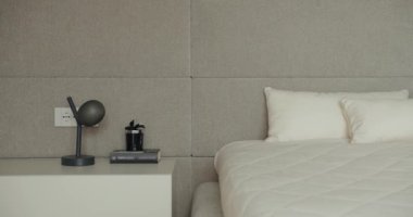 Mini minimalist bir yatak odası modern bir yatağın yanında şık bir lamba ve tertipli gri bir duvara dayalı dekorasyon sergiliyor. Tarafsız Tonlu ve Minimalist Dekorlu Modern Yatak Odası