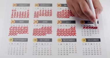 Ağustos ayının tamamlanmış aylarını ve güncel ilerlemesini gösteren, takvimdeki kırmızı haçlarla işaretlenen bir el işaretinin yakın plan çekimi. Ağustos ayı için Kızıl Haçlarla Takvimdeki El İşaretleme Tarihleri