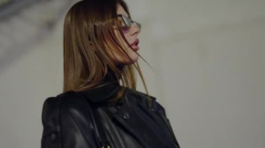 Deri ceket giyen genç bir kadın şık marka güneş gözlükleriyle fotoğraf çekimi için poz veriyor. Yüksek moda estetik modeli. Deri ceketli ve gözlüklü çekici bir kadın merdivenlerde dikiliyor..