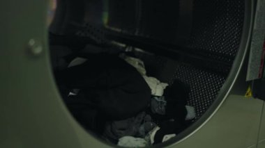 Çamaşırhanedeki çamaşır makinesinin içindeki kıyafetlerin detaylı bir görüntüsü. Temizliğin ve günlük ev işlerinin özünü yakalıyor. Çamaşır Tesisinde Endüstriyel Çamaşır Makinesi Kullanan Kişi