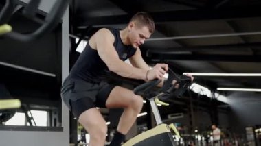 Ciddi bir genç erkek atlet, modern bir spor salonundaki kürek çekme makinesinde yoğun bir şekilde çalışıyor, azim ve güç gösteriyor. Spor salonunda kürek çeken genç adama odaklan.