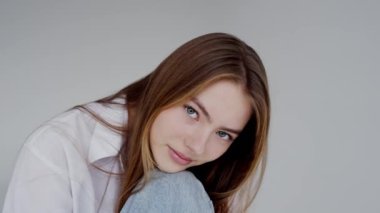 Çekici mavi gözleri ve nazik bir gülümsemesi olan genç bir kadının büyüleyici bir görüntüsü. O beyaz bir gömlek giyer ve eline yaslanır. Yoğun Mavi Gözlü Genç Kadının Yakın Çekim Portresi