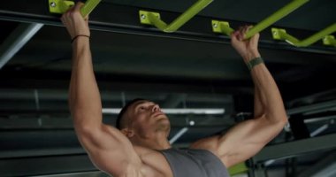 Genç kaslı bir adam spor salonundaki yeşil bir çubukta barfiks çekiyor. Formda olduğunu ve fiziksel gücünü gösteriyor. Güçlü Adam Modern Spor Salonunda Barfiks Çekiyor, Gücünü Gösteriyor