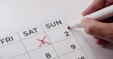 Bir takvime önemli bir tarihi işaretlemek için kırmızı işaret kullanan bir elin yakın çekimi. Bu resim zaman yönetimi, zamanlama, planlama ve önemli tarihleri temsil eder..