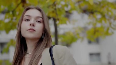 Açık havada, şehir parkının bulanık arka planında güz belirtileri gösteren günlük giysiler giymiş genç beyaz bir kadının yakın plan portresi. Genç Kadın Sonbaharda Açık Hava Poz Veriyor.