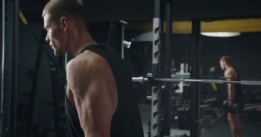 Kararlı genç bir erkek atlet, güçlü ve adanmışlığını yansıtan iyi donanımlı bir spor salonunda dambılları kaldırırken yoğun bir şekilde odaklanır. Modern Spor Salonu 'nda Ağırlık Kaldıran Genç Adam Odaklandı