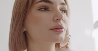 Tamamen pürüzsüz, sağlıklı cilde sahip güzel bir kadın yeşil yüz silindiri kullanarak masaj yaptırıyor. Evde güzellik tedavisi. Dermatoloji aletiyle cildine masaj yapan bir kadın..