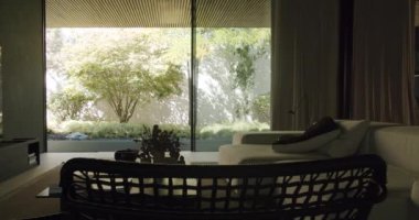 Huzurlu bir iç mekan, geniş cam bir pencereden panoramik manzaralı, yemyeşil bahçeli ve sakin ağaçlarla yıkanmış şık bir yaşam alanını gözler önüne seriyor. Modern Ev İçi