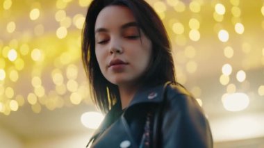 Siyah saçlı genç bir kadının yakın plan portresi, neşeli bokeh ışıklarıyla aydınlatılmış, sıcak ve büyüleyici bir atmosfer yaratıyor. Arka planda Neşeli Işıkları Olan Genç Kadın Portresi