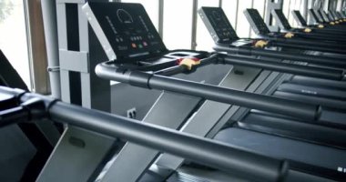 Modern bir spor salonunda bir dizi ileri koşu bandı düzgün sıralanmış, doğal manzaralı bir pencereye bakıyor. Fitness teknolojisi ve spor salonu atmosferine odaklan.