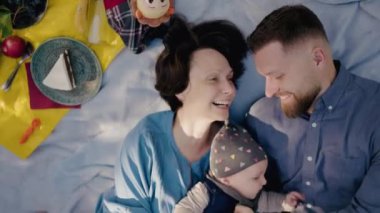 Genç bir ailenin piknik sırasında sevgisini ve gülümsemesini paylaştığı yürek ısıtan bir sahne. Görüntü onların neşeli bir bebekle bağlanma anlarını yakalıyor. Neşeli Aile Bebekleriyle Dışarıda Piknik Yapıyor