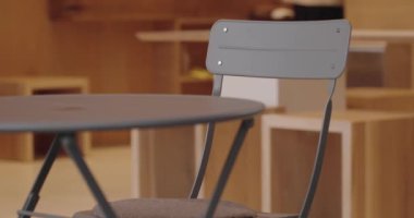 Modern gri bir sandalye ve uyumlu bir masayı gösteren şık bir kafe ortamının canlı görüntüsü. Bu minimalist tasarım modern yaşam ve kafelerle ilgili konular için ideal çağdaş bir atmosferi çağrıştırıyor.